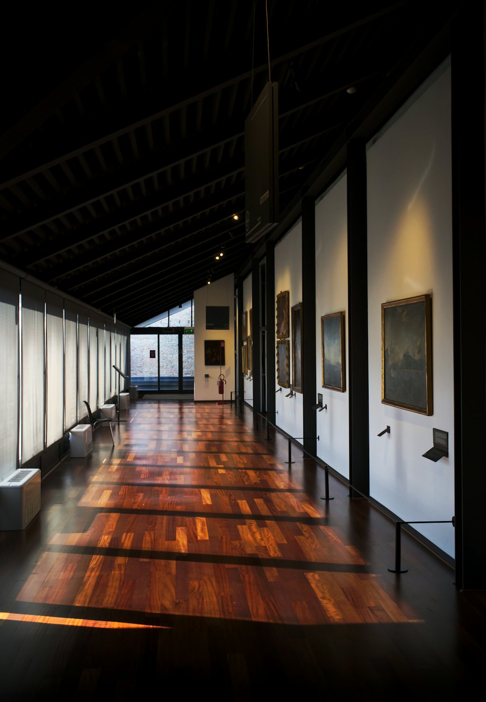 Pasillo vacío de galería de arte con cuadros en paredes blancas.