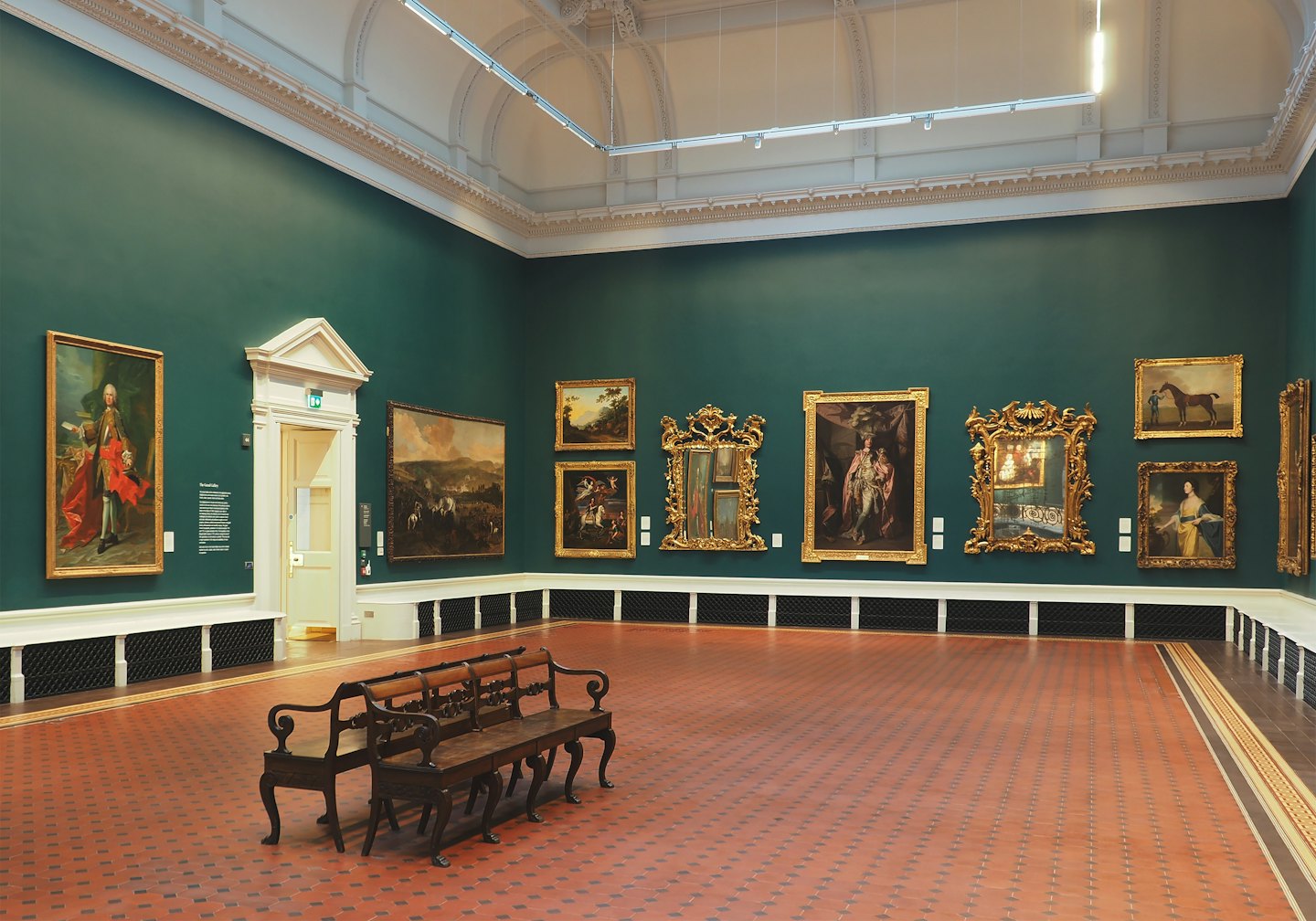 Pinturas ornamentadas cuelgan en las paredes de la galería sobre bancos de madera.