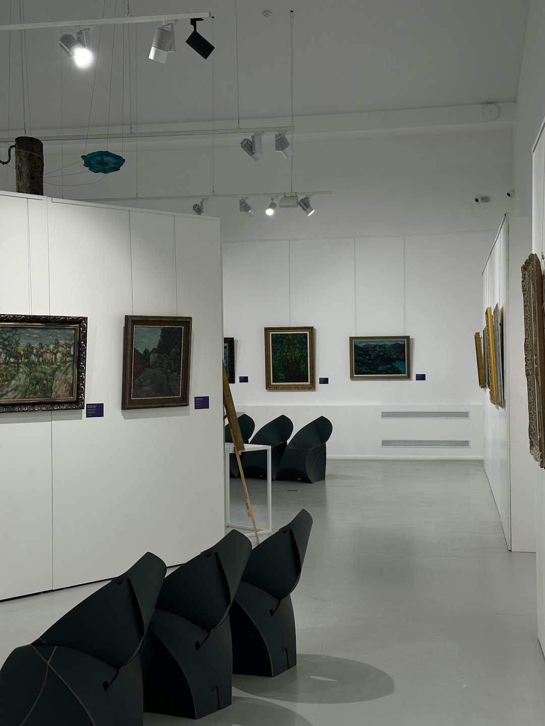 Galería de arte moderno con pinturas de paisajes y esculturas colgantes.